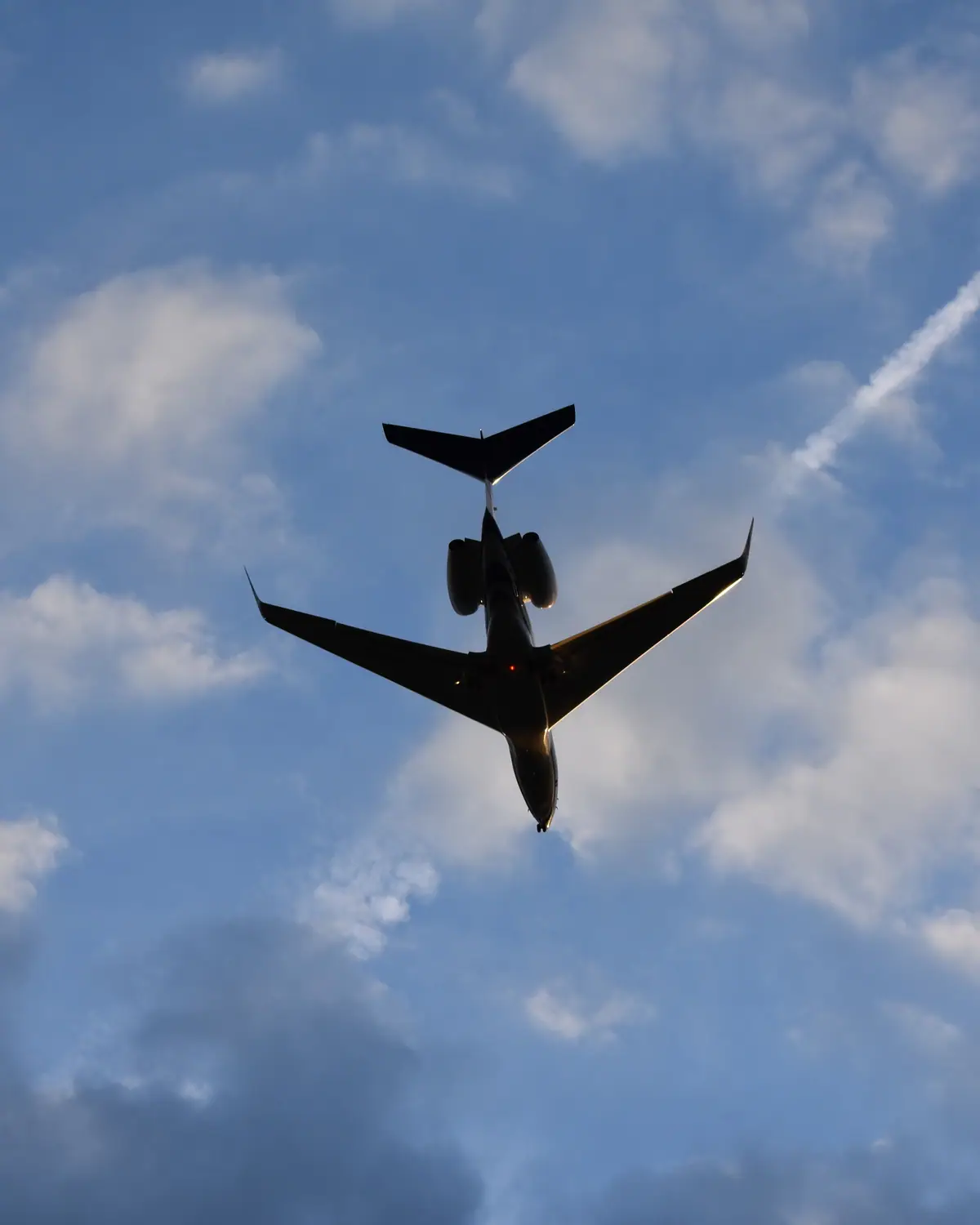 Business jet passing overhead against a blue sky with scattered clouds